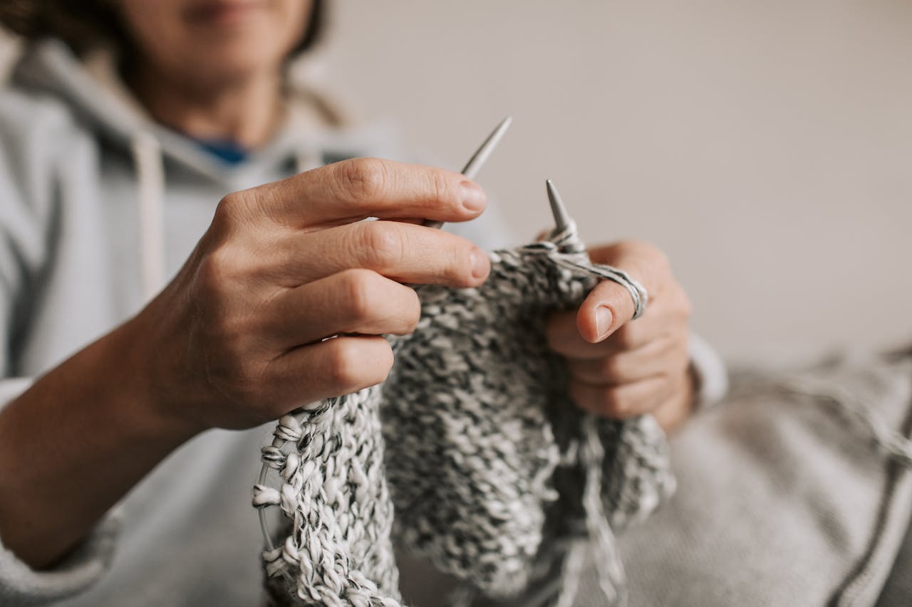 Close-up of hands engaged in knitting with needles, showcasing knitting hobby indoors.